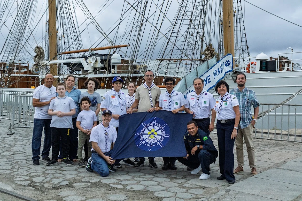 Integrantes do 5º AL reunidos diante de um veleiro, com a bandeira do grupo